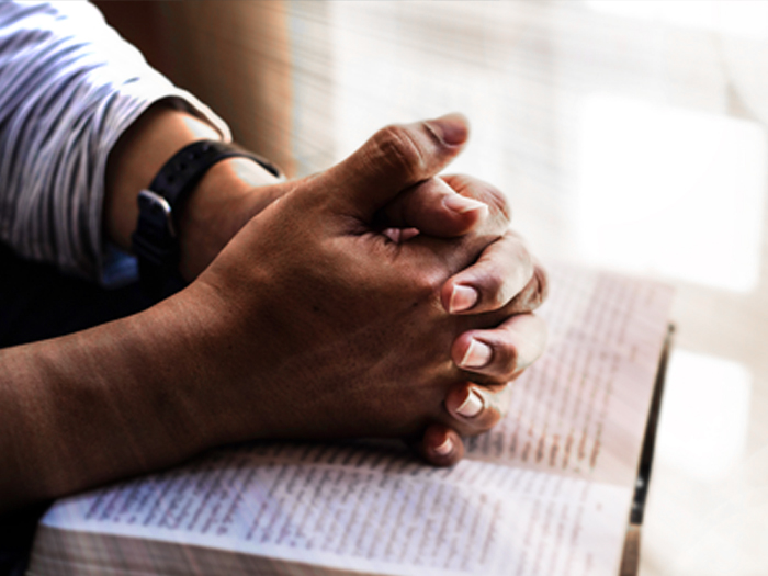 Folded Hands in Prayer Position on open Bible